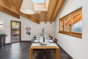 A dining area with a wooden table set for four, a large window with wooden shutters, and a skylight above.