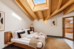 A bedroom with a wooden ceiling, a bed with white bedding, a bedside table, and a view of the outside.