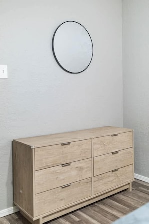 A wooden dresser with drawers against a wall, a round mirror above it, and a light switch to the left. - Charming 2BR Apartment in Central Lawton Near Fort Sill (Lawton)