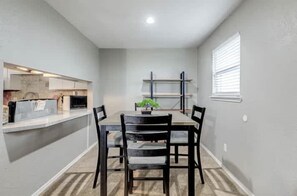 A dining area with a table and chairs, a kitchen counter, and a window with blinds. - Charming 2BR Apartment in Central Lawton Near Fort Sill (Lawton)