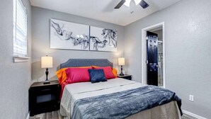 Une chambre à coucher comprenant un lit, deux tables de chevet, un ventilateur de plafond et des œuvres d’art accrochées au mur.