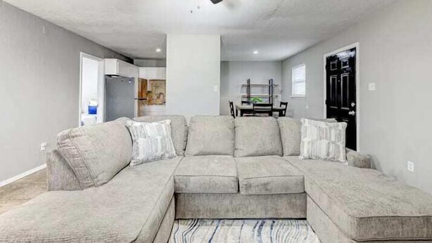 Un salon avec un canapé d’angle, un ventilateur de plafond et un coin repas à l’arrière-plan.