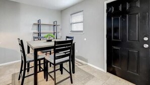 Un coin repas avec une table et des chaises, une petite fenêtre avec des stores et une porte noire.