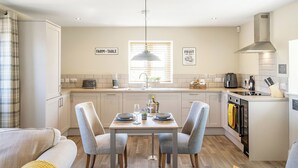 Une cuisine moderne avec une table à manger pour quatre personnes, un four encastré et une grande fenêtre avec des stores.