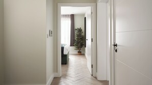 A hallway with a herringbone floor leading to a room with a bed and a potted plant. - Commercial Road Serviced Apartments - London City East (London)