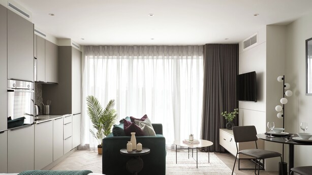 A modern hotel room with a kitchenette, a green sofa, a dining area with a table and chairs, and a large window with curtains. - Commercial Road Serviced Apartments - London City East (London)