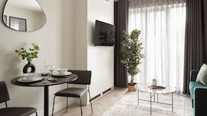 A modern living room with a dining area, a flat-screen TV mounted on the wall, a potted plant, and a sofa. - Commercial Road Serviced Apartments - London City East (London)