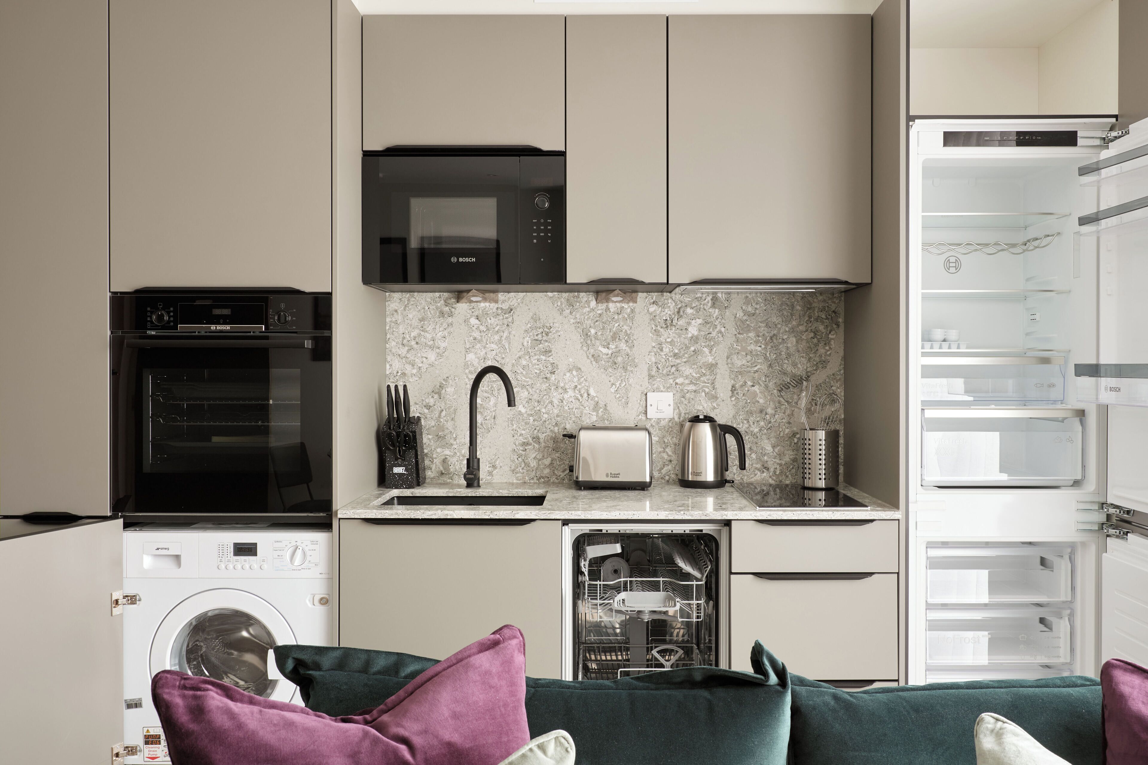 Una cocina compacta con microondas Bosch, tostadora y lavavajillas, lavadora y refrigerador con varios compartimentos.
