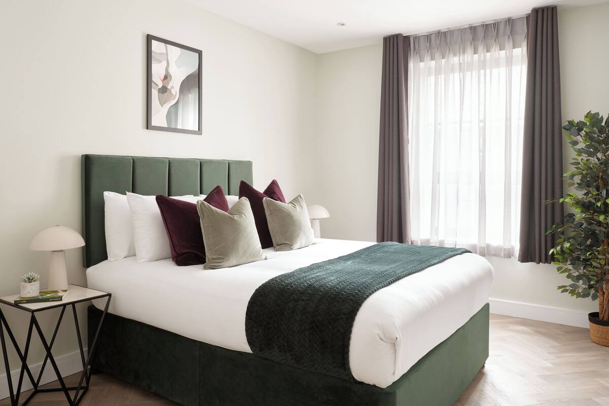 Ein modernes Schlafzimmer mit einem grünen, bezogenen Bett, weißer Bettwäsche und einem Nachttisch mit einer Lampe.