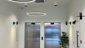 A modern elevator area with two elevators, a herringbone-patterned floor, and a potted plant. - Commercial Road Serviced Apartments - London City East (London)