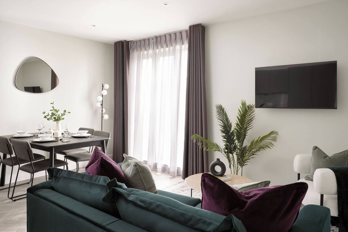 Een moderne woonkamer met een bank, eettafel en een flatscreen televisie aan de muur.