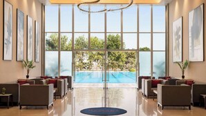 A modern lobby with a pool view, comfortable seating, and artwork on the walls. - Ramada by Wyndham Ahmedabad Narendra Modi Stadium Motera (Ahmedabad)