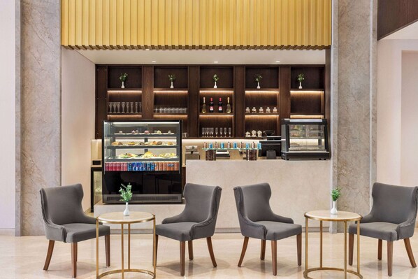 Un vestíbulo moderno con zona de bar, asientos y una vitrina con alimentos.