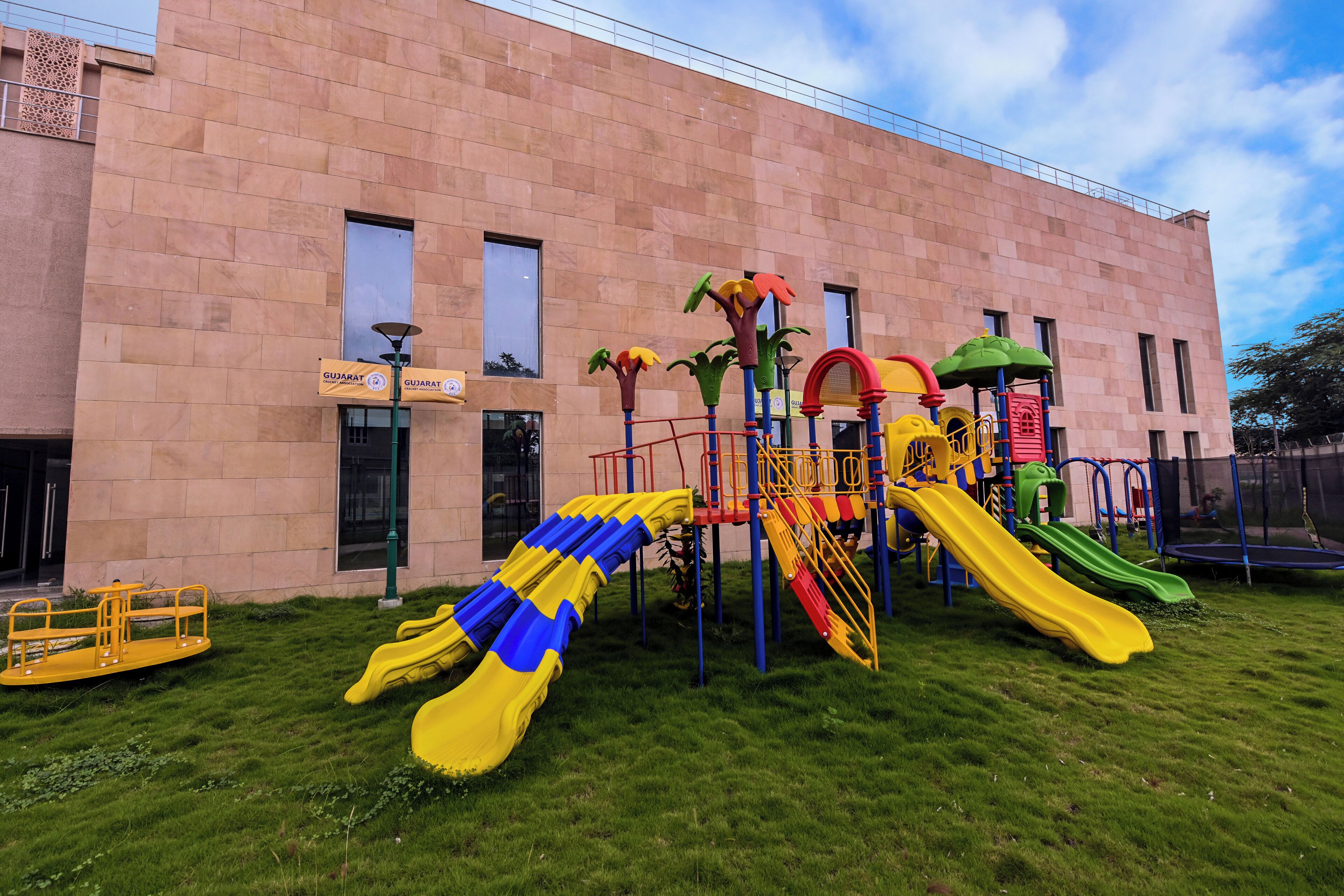 A playground with slides and climbing structures in front of a building with banners.