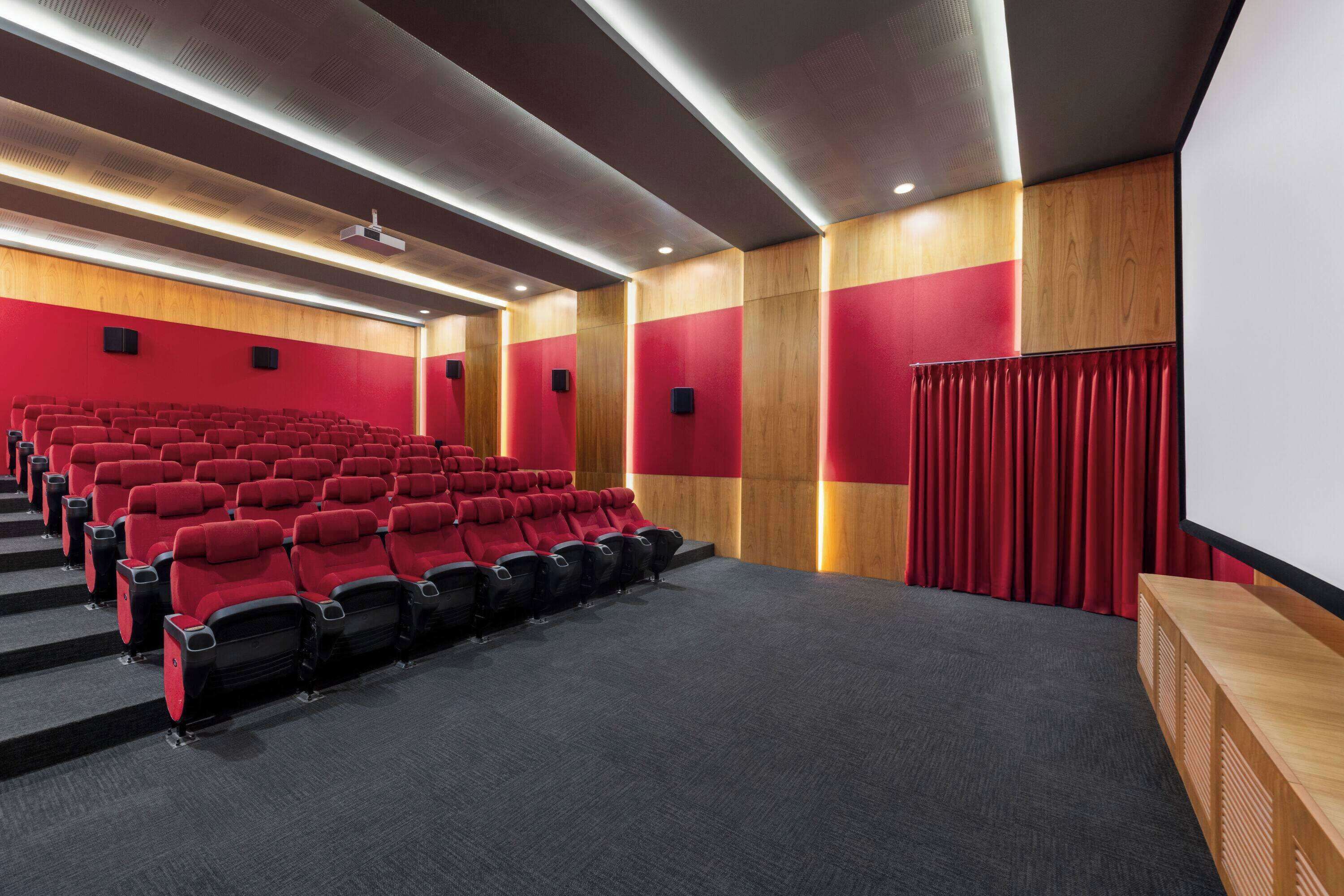 Un cine con asientos rojos, paneles de madera y una pantalla grande.