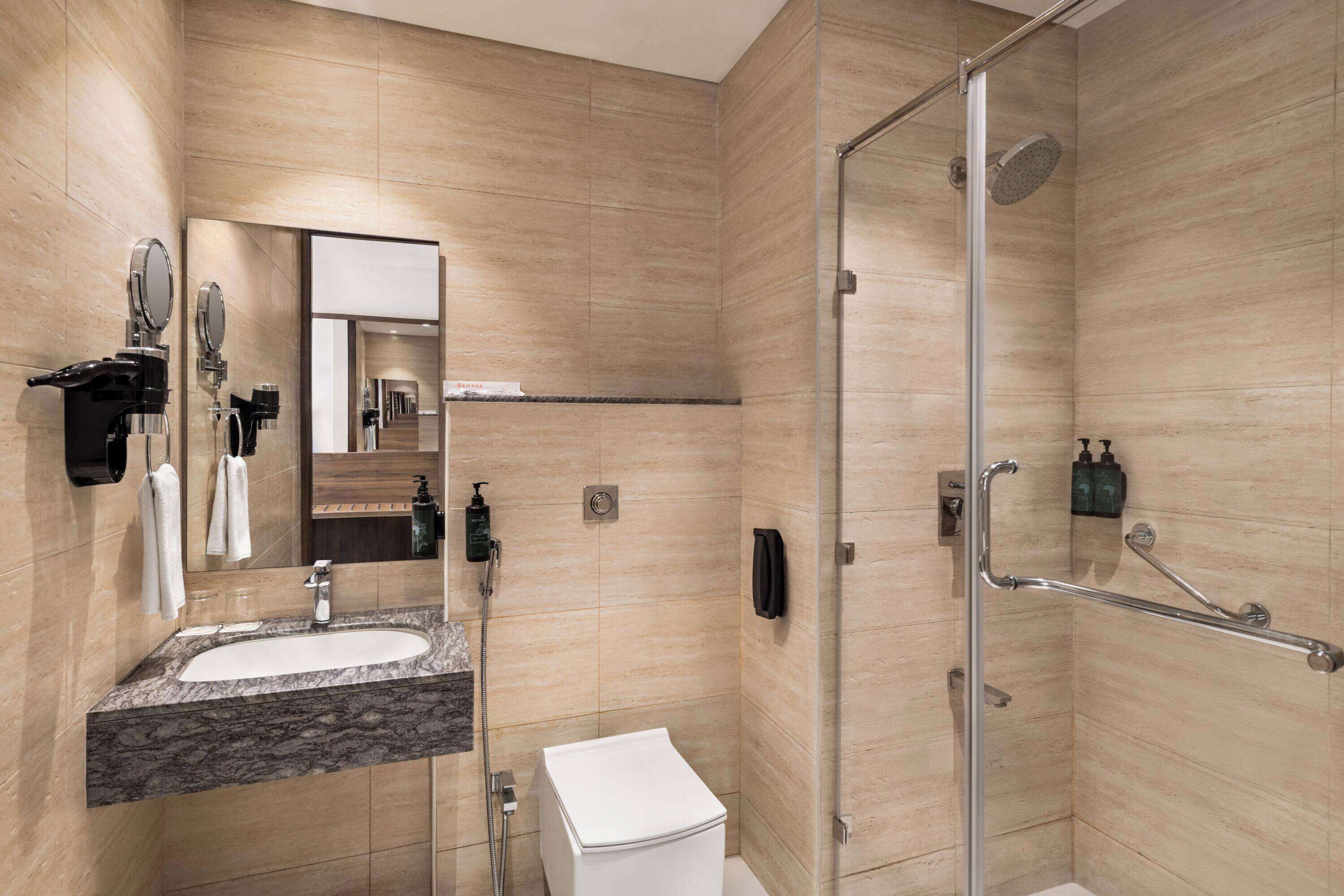 Une salle de bain moderne avec un lavabo en marbre, des toilettes, une douche en verre avec un pommeau de douche à main et un miroir à main.