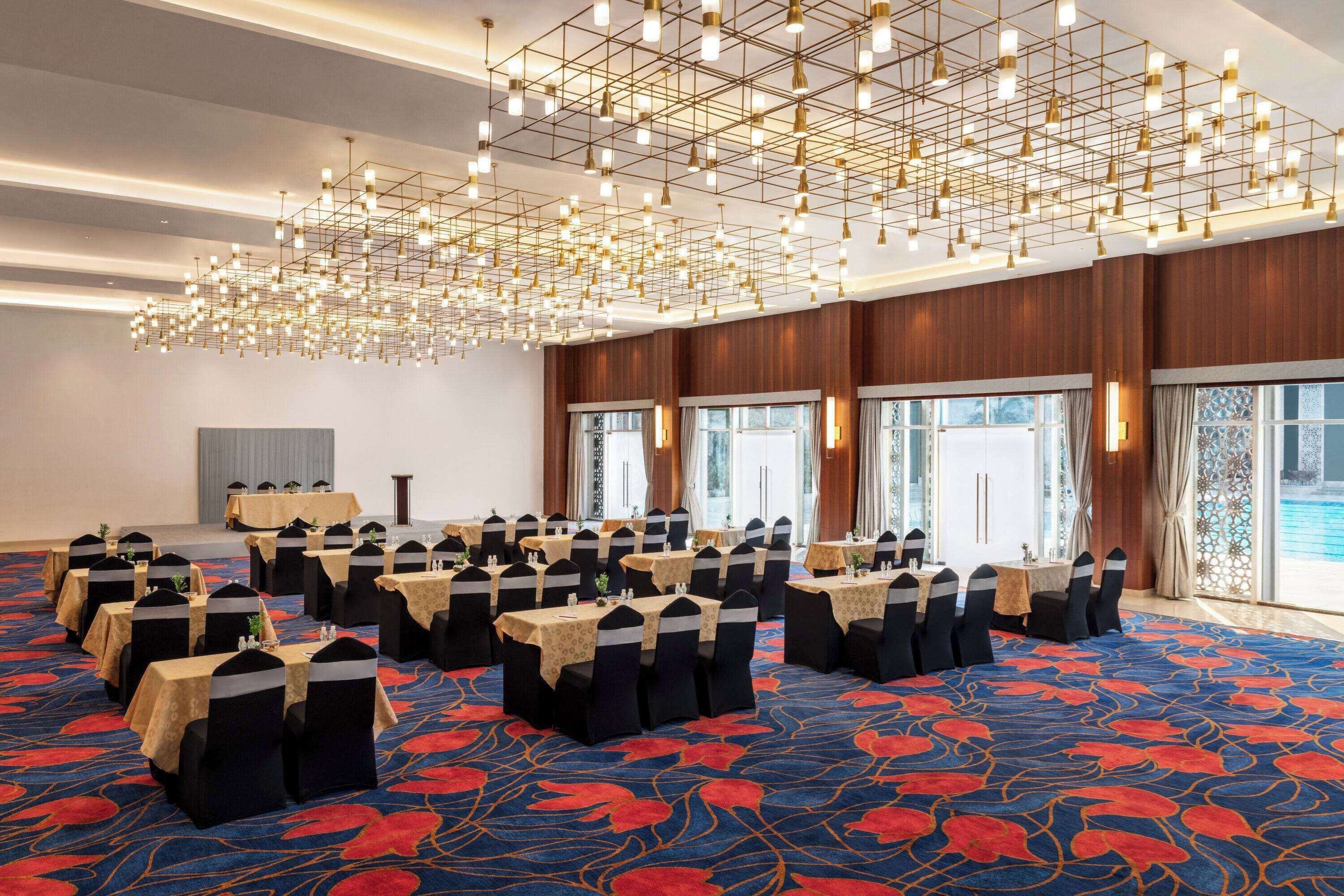 Una sala conferenze con vari tavoli e sedie, un tappeto decorato e un lampadario moderno.