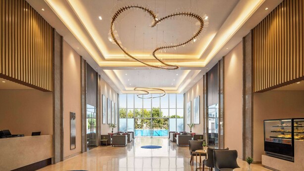 A spacious lobby with a reception desk, seating area, and a large window offering a view of the outdoors. - Ramada by Wyndham Ahmedabad Narendra Modi Stadium Motera (Ahmedabad)