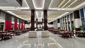 A spacious hotel lobby with a central reception desk, multiple dining areas with tables and chairs, and large windows providing natural light. - Ramada by Wyndham Ahmedabad Narendra Modi Stadium Motera (Ahmedabad)