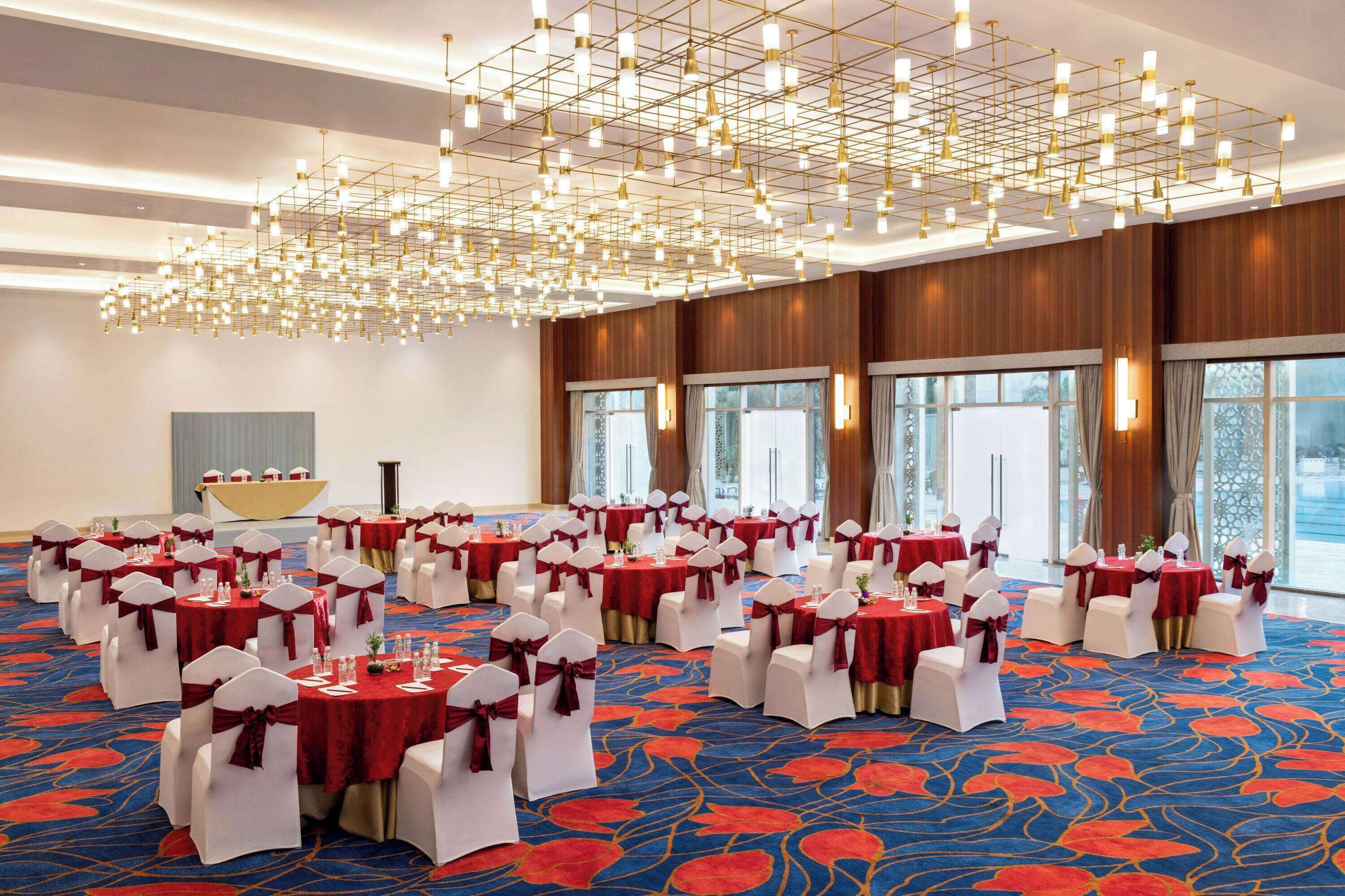 A banquet hall with round tables, white chairs, and red tablecloths.