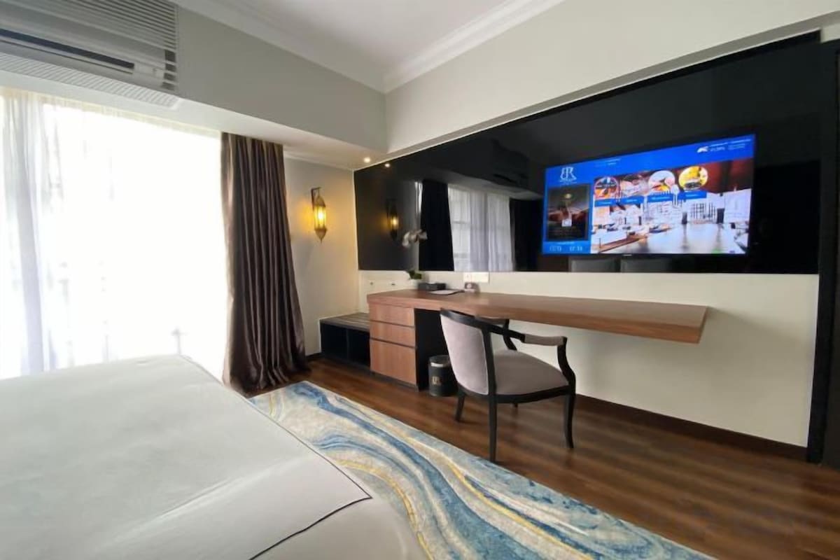 Una habitación de hotel con cama, escritorio, silla, televisor y ventana con cortinas.