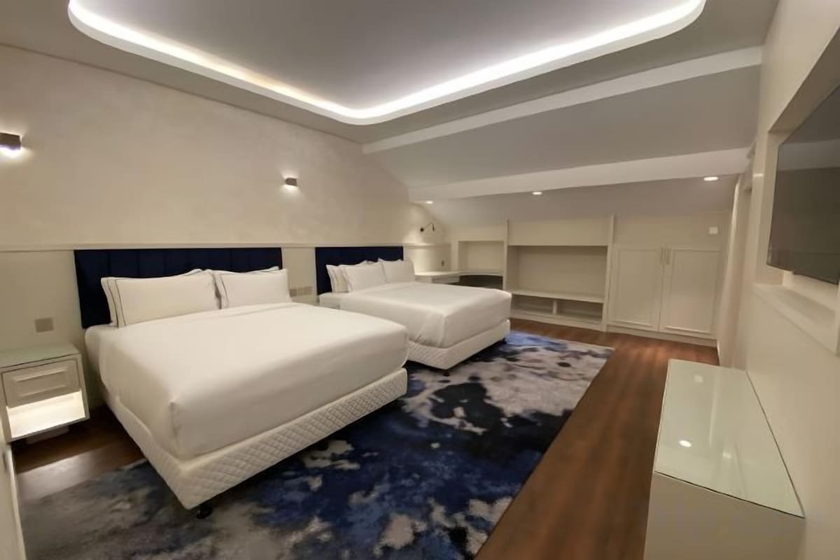 A modern bedroom with two beds, a large mirror, and a TV.
