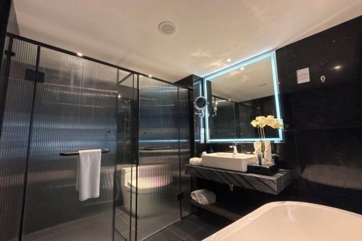 A modern bathroom with a glass-enclosed shower, a large mirror, a white sink, and a bathtub.