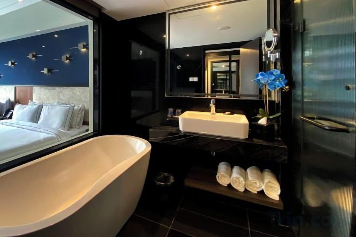 A modern bathroom with a large bathtub, a vanity with a mirror, and a shelf with towels.