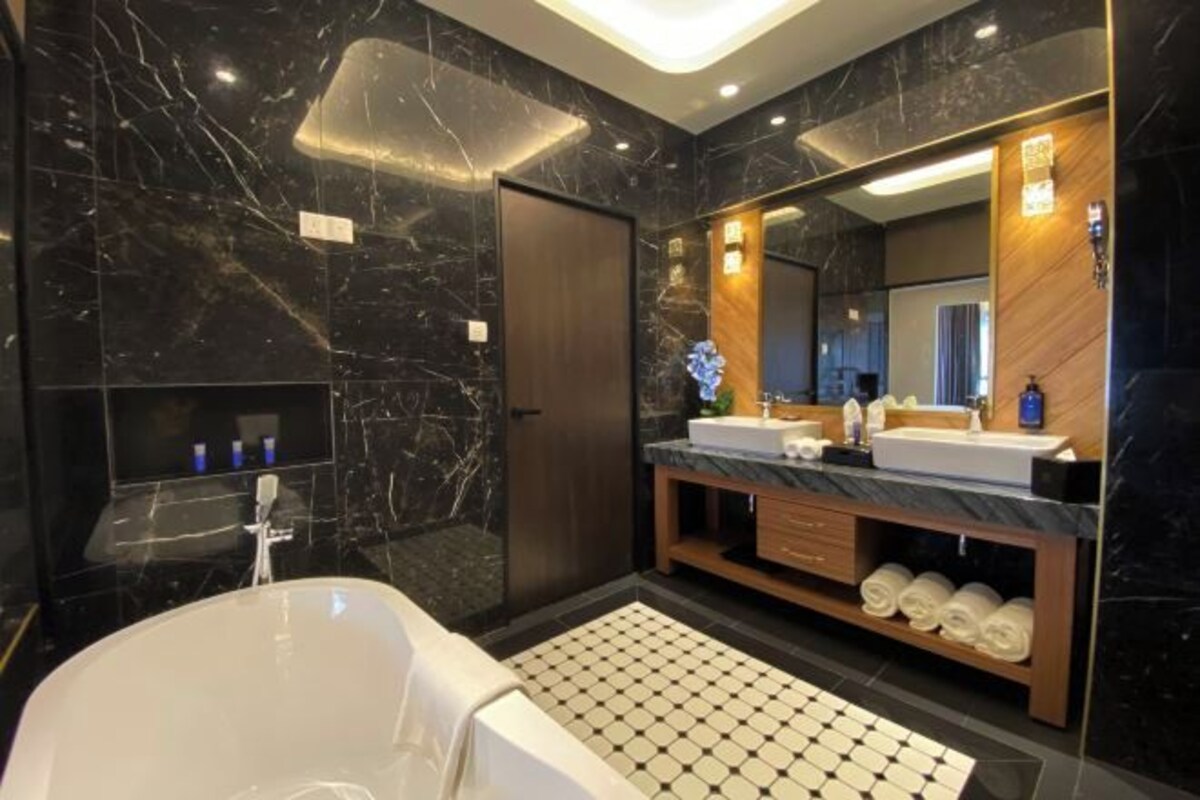 A modern bathroom with a marble wall, a freestanding bathtub, a vanity with a mirror, and a wooden shelf with towels.