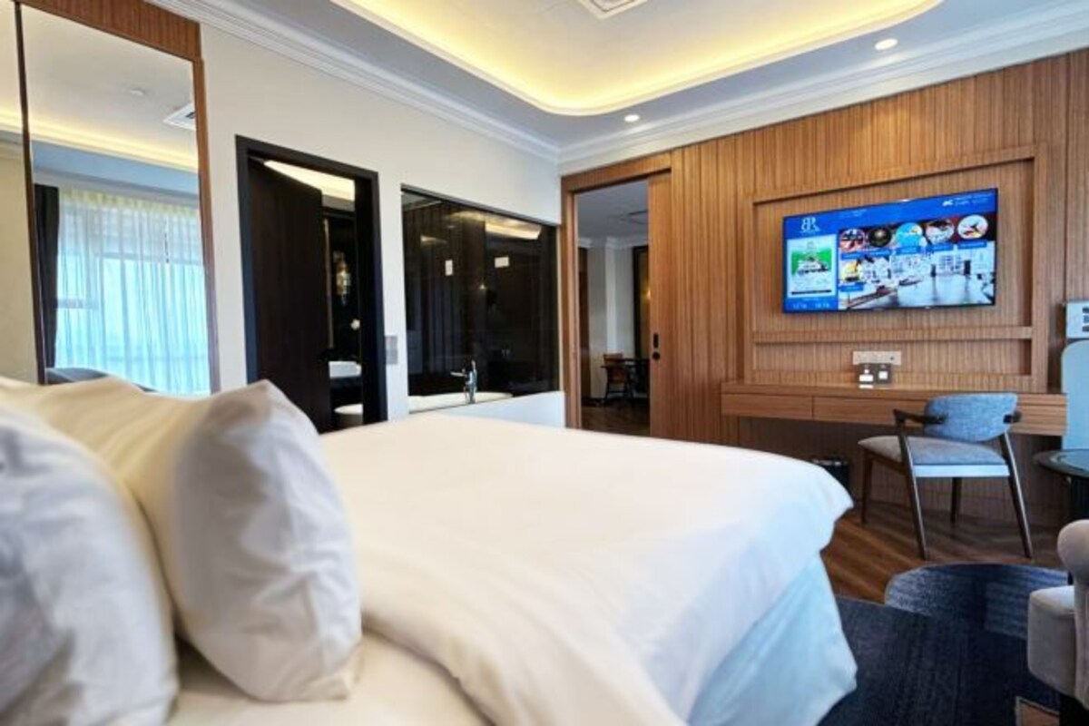 A hotel room with a large bed, a TV mounted on the wall, a desk, and a chair.