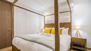 Un lit à baldaquin avec du linge de lit blanc, une tête de lit en bois et deux lampes de chevet.
