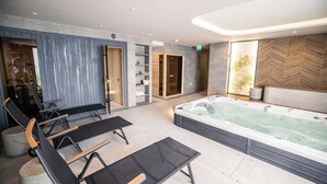 Een moderne spa-ruimte met een ruime jacuzzi, zwarte loungestoelen en een houten wand met planken.