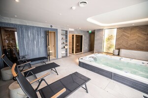 Uma área de spa moderna com uma grande banheira de hidromassagem, cadeiras de descanso pretas e uma parede de madeira com prateleiras.