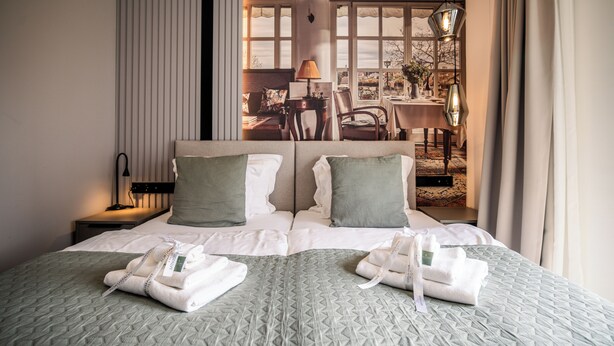 Hotelkamer met een groot bed, twee kussens, een nachtkastje met lamp en uitzicht op het buitenterras.