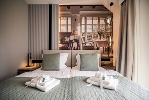 Quarto de hotel com uma cama grande, duas almofadas, mesa de cabeceira com abajur e vista para a área de estar externa.
