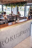 Zona de recepción con mostrador de mármol que dice "RÖKUSFALVY", con una botella de vino y una copa, y vistas al exterior a través de amplias ventanas.