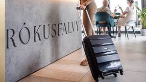 Een receptiebalie met een bord waarop 'RÖKUSFALVY' staat en een vrouw met bagage.