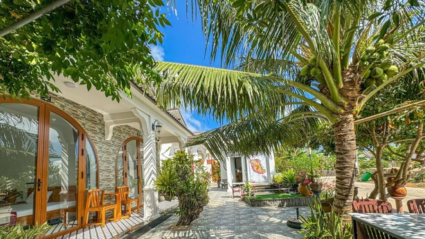 A courtyard with a stone floor, wooden furniture, and tropical plants. - BA DUNG VILLA Coffee (Phu Quy)