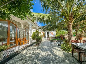 A courtyard with a stone floor, wooden furniture, and tropical plants. - BA DUNG VILLA Coffee (Phu Quy)