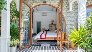 A hotel room with a bed, a small table, a nightstand, a potted plant, and a view of the outside. - BA DUNG VILLA Coffee (Phu Quy)