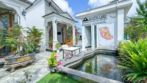 A traditional house with a tiled roof, a stone pathway, a small pond with koi fish, and a signboard. - BA DUNG VILLA Coffee (Phu Quy)