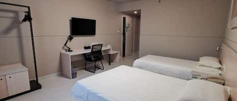 A hotel room with two beds, a desk with a chair, a TV, and a wardrobe.