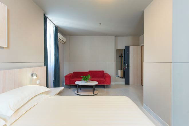 A modern hotel room with a bed, a red sofa, a small round table, and a plant.