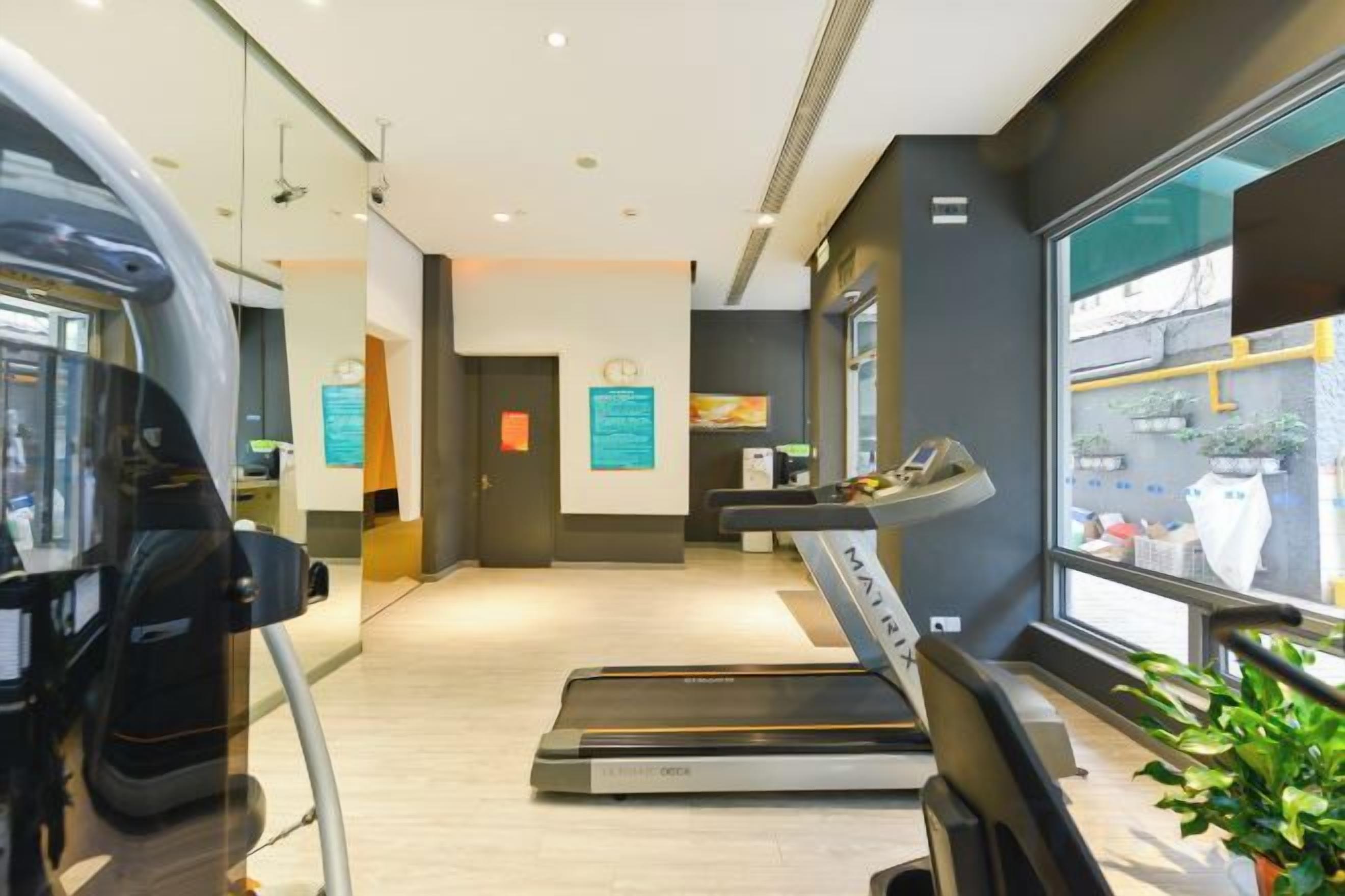 Academia com esteiras e equipamentos de ginástica, um balcão de recepção e vista para a rua.