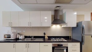 A modern kitchen with white cabinets, a built-in oven, a stove, and a refrigerator. - Comfy Studio Apartment in DIFC (DIFC)