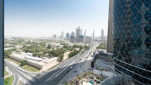 A high-rise building with a modern glass facade, a wide road with vehicles, and a distant city skyline. - Comfy Studio Apartment in DIFC (DIFC)
