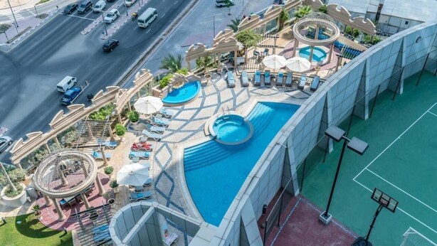 An aerial view of a hotel with multiple swimming pools, a tennis court, and a road with vehicles. - Comfy Studio Apartment in DIFC (DIFC)