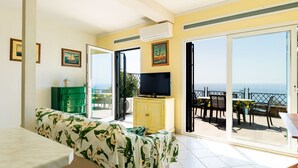 Une chambre avec un lit, une télévision, une armoire verte et un balcon équipé d’une table et de chaises.