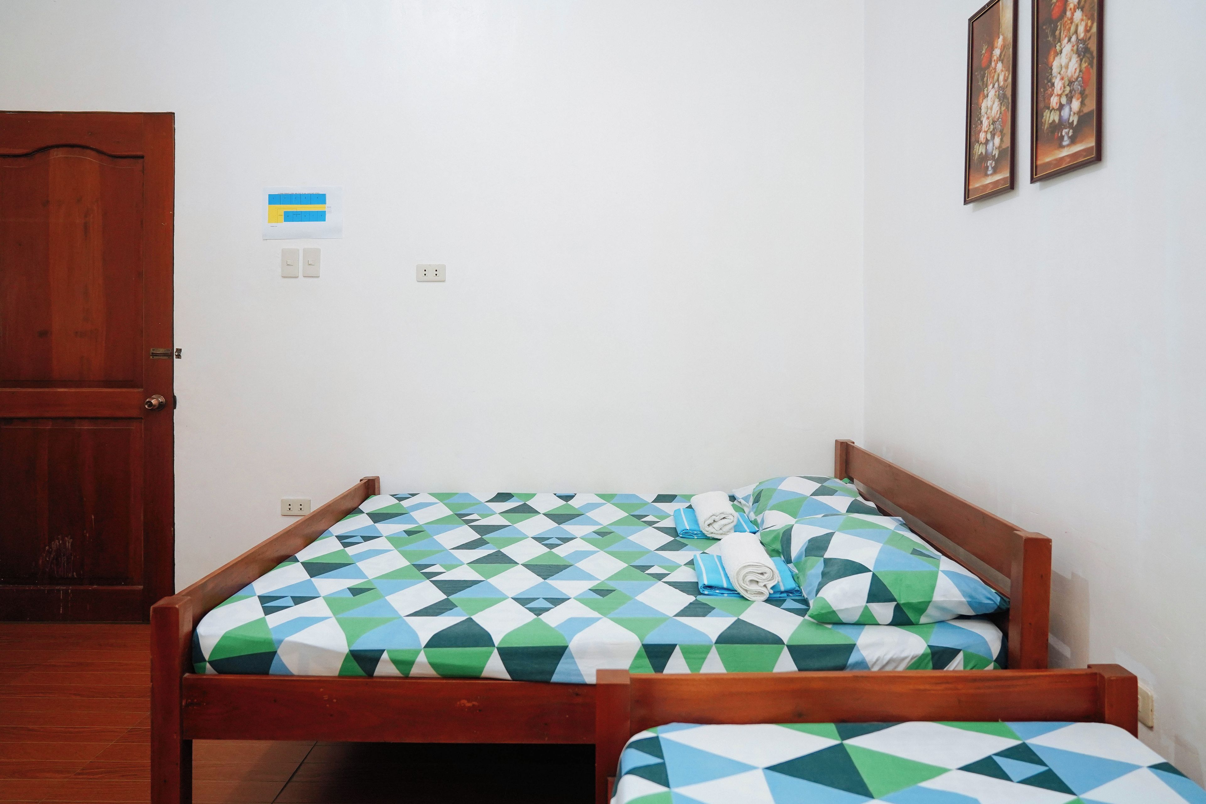 A room with two wooden beds, a wooden door, and a wall with a flag and two framed pictures.