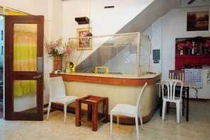 A small bar area with a wooden counter, two white wicker chairs, a small wooden table, and a red cloth-covered shelf with bottles. - C Star Travellers Inn Redpartner (Oslob)
